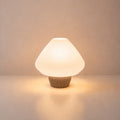 Abajur de mesa Lotus aceso, com cúpula branca plissada e base capuccino