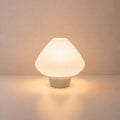 Abajur de mesa Lotus aceso, com cúpula branca plissada e base caucasiano