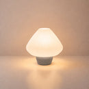 Abajur de mesa Lotus aceso, com cúpula branca plissada e base cinza claro