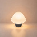 Abajur de mesa Lotus aceso, com cúpula branca plissada e base grafite