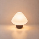 Abajur de mesa Lotus aceso, com cúpula branca plissada e base marrom