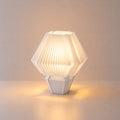 Abajur de mesa aceso, com cúpula branca hexagonal plissada e base branca