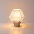 Abajur de mesa aceso, com cúpula branca hexagonal plissada e base capuccino