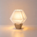 Abajur de mesa aceso, com cúpula branca hexagonal plissada e base capuccino