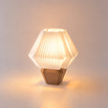 Abajur de mesa aceso, com cúpula branca hexagonal plissada e base caramelo